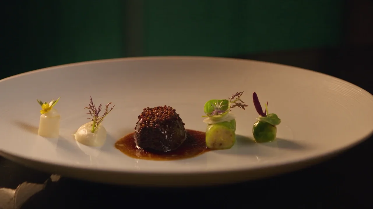 Een chef legt met een pincet de laatste kruiden op een verfijnd gerecht
